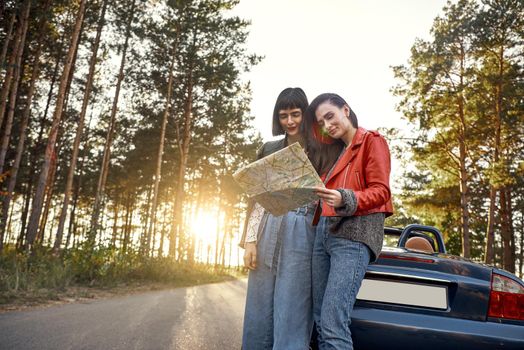 Two women trying to find the way on map near roofless rental car traveling during roadtrip