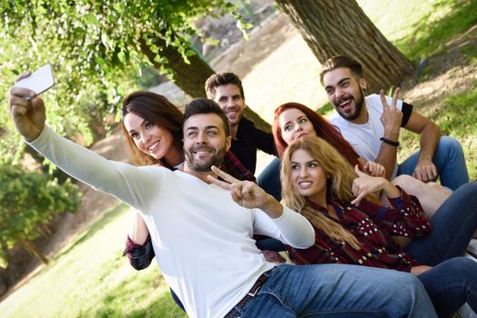 Group of friends taking selfie in urban park. Five young people wearing casual clothes.