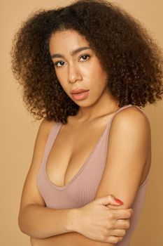 Portrait of attractive mixed race young woman with curly hair looking at camera while posing, standing isolated over light background. Natural beauty, skincare concept