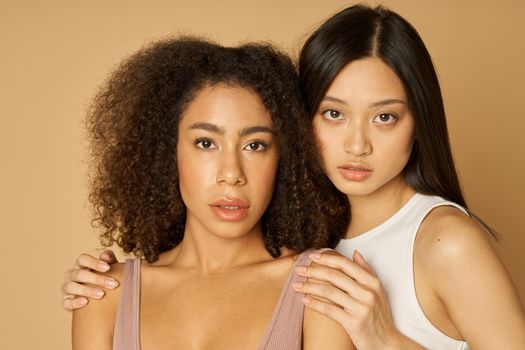 Portrait of two stunning mixed race young women with perfect skin looking at camera while posing together isolated over light background. Female beauty portrait. Front view