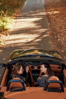 Rear view of two women friends in cabliolet. They are laugthing and talking. Happy journey