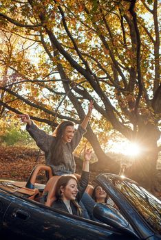 Portrait of three pretty young women driving on road trip on beautiful autumn day.