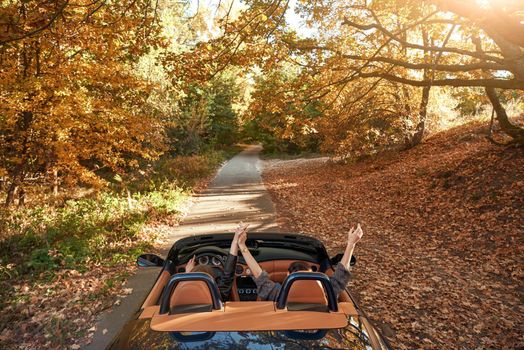 Female friends driving cabriolet with the hands up and having fun on the vacation