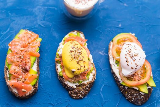 Sandwiches with smoked salmon, eggs, sauce and avocado on blue background. Concept of breakfast and healthy nutrition