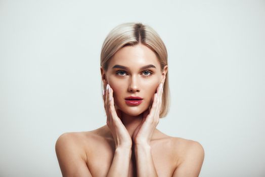 Confident in her beauty. Sexy young woman with blond hair and perfect shiny skin looking at camera while standing against grey background. Women beauty. Skin care. Studio shot