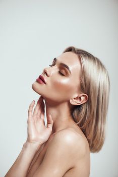 Pure beauty. Profile portrait of gorgeous young woman with blond hair and perfect shiny skin keeping eyes closed while standing against grey background. Women beauty. Skin care. Studio shot