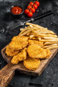Chicken nuggets with ketchup and French fries on wooden board. Black background. Top view.