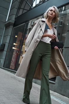 Fashion. Young stylish woman walking on the city street looking aside curious full body shot