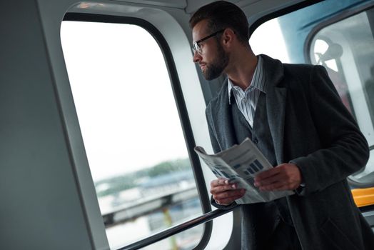 Business trip. Young businessman standing in the train holding newspaper looking out the window enjoying window view