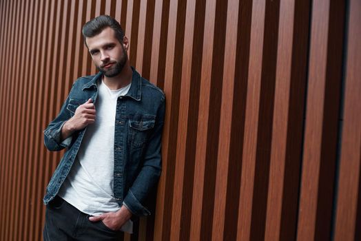 Freestyle. Young man standing leaning on wooden wall isolated looking camera smiling playful