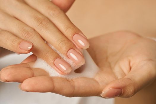 Close up of female hands holding, applying gentle foam facial cleanser. Beauty products and skin care concept