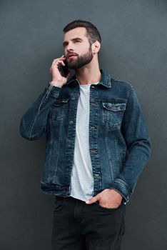 Freestyle. Young man standing isolated on grey wall hand in pocket talking on smartphone confident