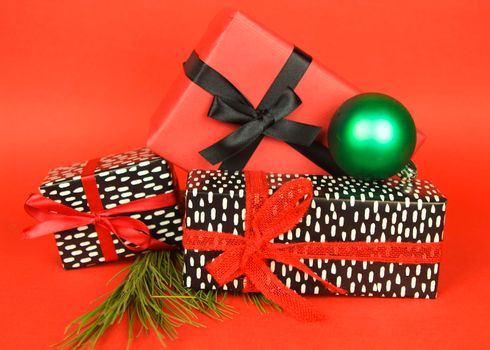Gifts wrapped with colorful paper and red and black bows next to Christmas decoration on red background