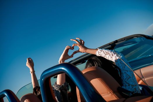 Female friends driving cabriolet with the hands up and having fun on the vacation