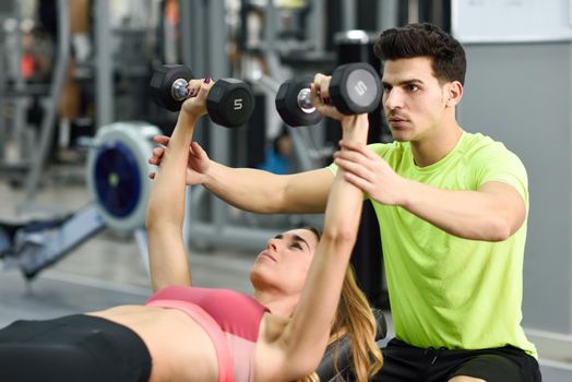 Personal trainer helping a young woman lift weights while working out in a gym