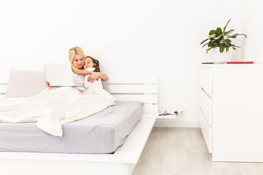 Smiling mother and daughter using laptop in bed at home