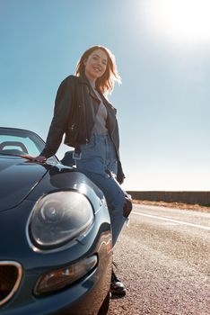 Young woman near roofless car and smiling outdoors on sunny day near the empty road. No people, sportive black car