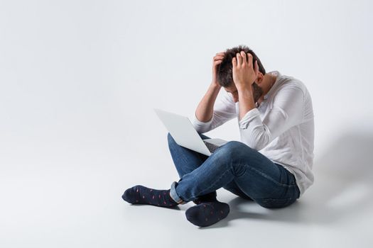 a young man in casual clothes working on a laptop. frustrated his head in his hands