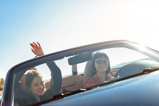 Female friends driving cabriolet with the hands up and having fun on the vacation