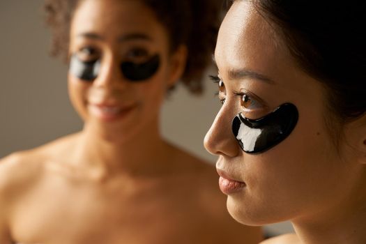 Close up portrait of two mixed race young women posing with applied black under eye patches. Beauty treatment concept. Selective focus