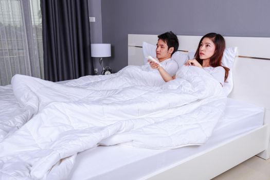 young couple lying on a bed with remote control of air conditioner in the bedroom