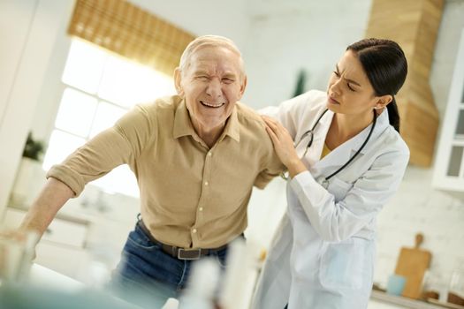 Concerned female doctor furrowing her brow while helping senior man to get up from the chair