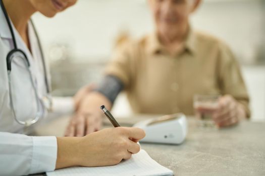 Selective focus photo of busy doctor taking notes in medical history of a senior citizen