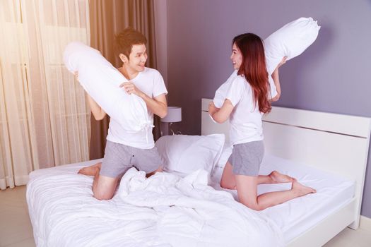 cheerful young couple having a bolster pillow fight on bed in the bedroom