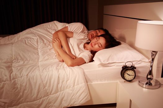 young couple hugging and sleeping on bed at night