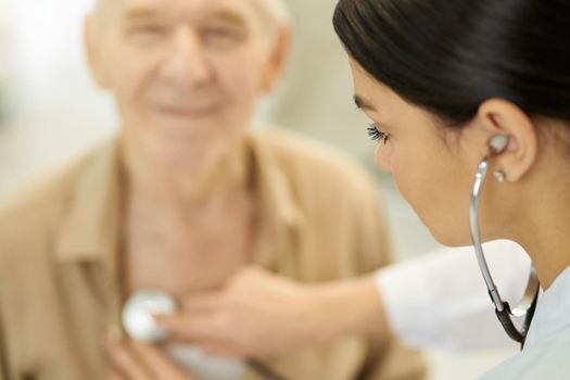 Selective focus photo of a concentrated female doctor using stethoscope to examine senior citizen lungs and heart