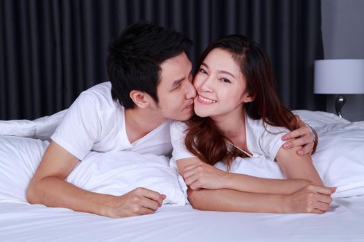 young man is kissing his beautiful smiling wife in cheek on bed