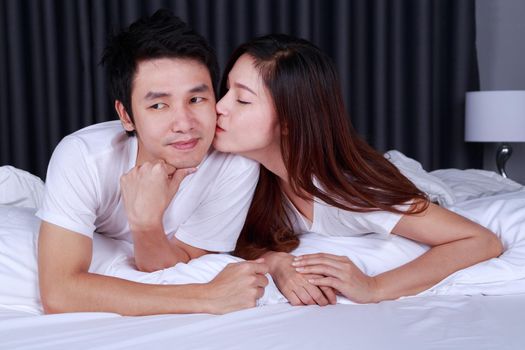 young woman is kissing her husband in cheek on bed
