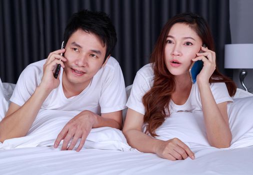 young couple lying in bed and talking on mobile phone