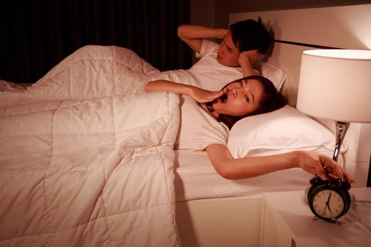 unhappy couple being awakened by an alarm clock in bedroom in the morning