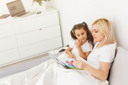 mother and daughter in bed watching a photo book