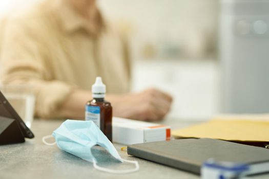 Cropped photo of surgical mask and a bottle of sanitizer sitting on the table of an elderly man