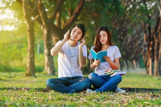 young couple reading a book and listening music with headphone in the park
