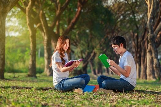 man and woman sitting and reading a book in the park