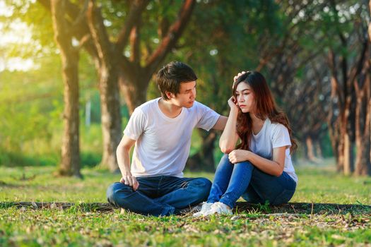 unhappy woman sitting with a concerned guy comforting her in the park