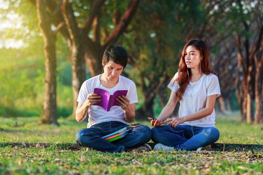 young couple reading a book and listening music with earphones in the park