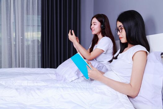 two woman reading a book and using smart phone on bed in the bedroom