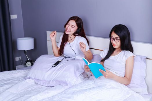 two woman reading a book and using smart phone on bed in the bedroom