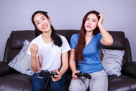 two young woman using joystick controller playing video game on sofa in living room at home