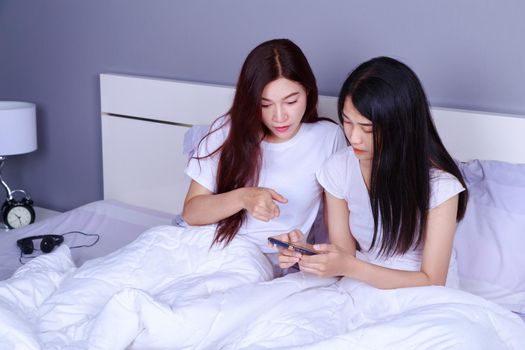 two woman using a phone in her hand on bed in the bedroom