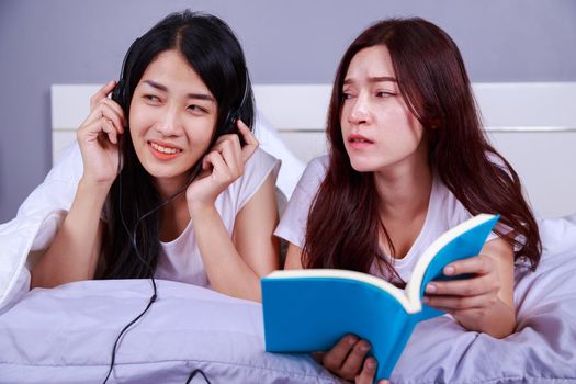 two woman reading a book and using smart phone on bed in the bedroom