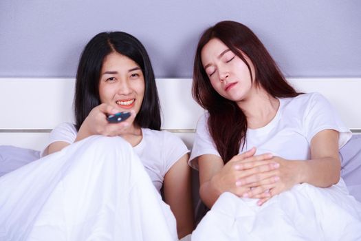 woman watching a television while her friend is sleeping on the bed