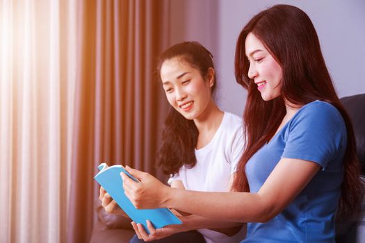 two young woman reading a book on sofa in living room at home