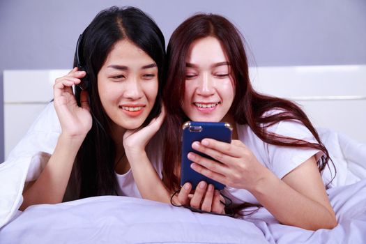two woman using a phone in her hand on bed in the bedroom