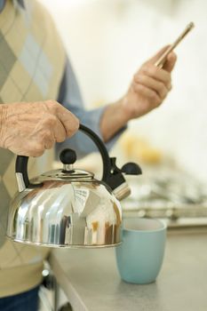 Cropped photo of man with smartphone in hand pouring water out of a kettle
