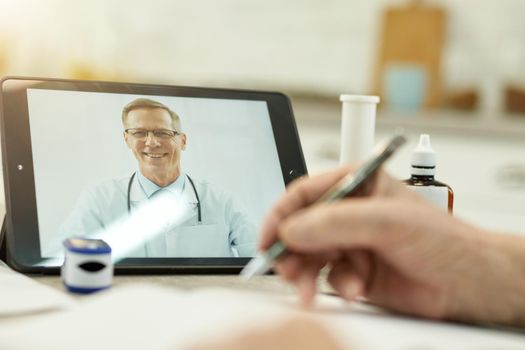 Cropped photo of person making notes while having a medical consultation with a friendly doctor online